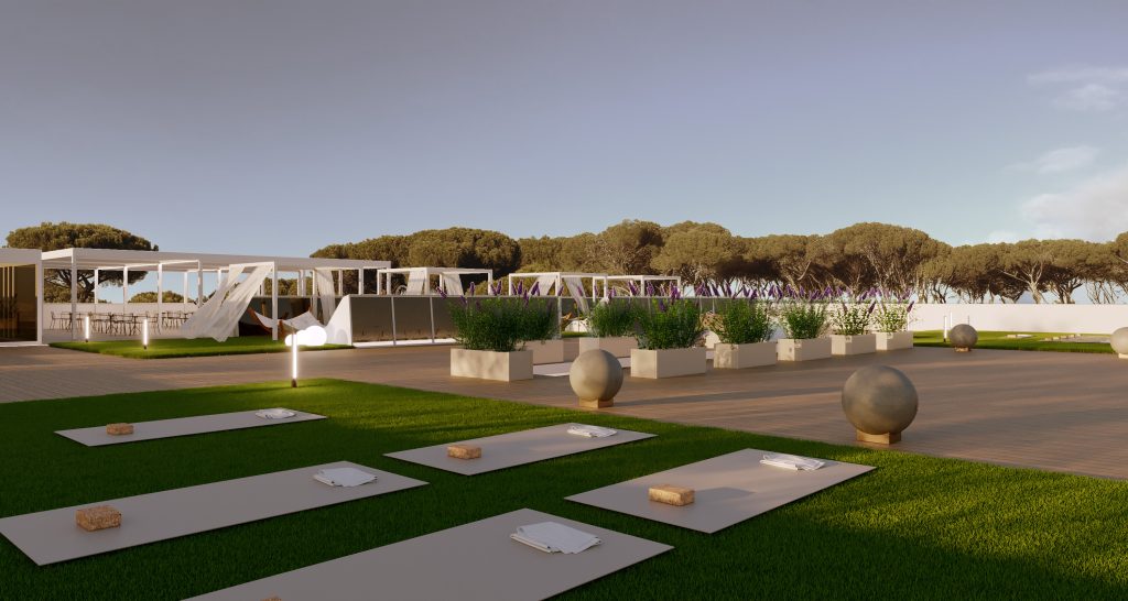 Una moderna area yoga all'aperto con tappetini e blocchi sull'erba verde, circondata da fioriere e sfere decorative, con un'area salotto ombreggiata e alberi sullo sfondo sotto un cielo limpido.